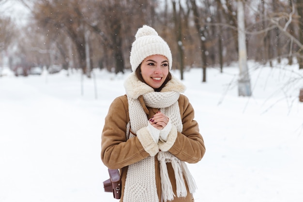 冬の雪の中で屋外を歩く帽子とスカーフの美しい若い女性の肖像画。