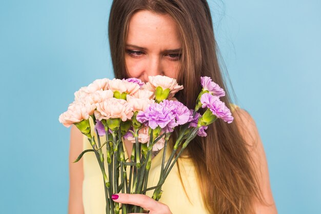 Ritratto di bella giovane donna che tiene un mazzo di fiori di garofano su sfondo blu, femminile, celebrazione