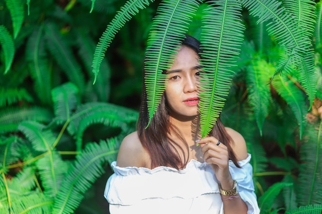 Portrait of beautiful young woman holding fern leaves in forest