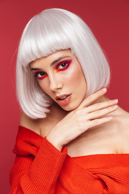 Portrait of beautiful young woman isolated on red wall with bright makeup posing.