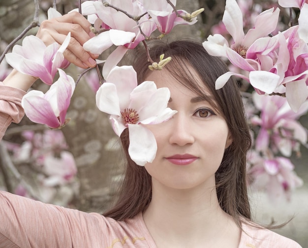 Portrait of beautiful young woman in japanese garden with blooming pink magnolia flowers