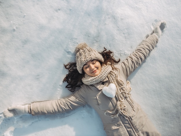 Portrait of a beautiful young woman laying down on a frozen snow lake during a sunny winter vacation