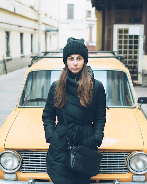 Foto ritratto di una bella giovane donna appoggiata a un'auto parcheggiata in strada