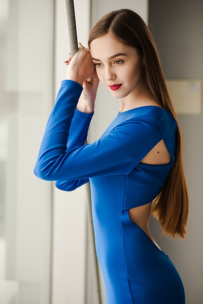 Портрет красивой молодой женщины в длинном голубом платье возле окна