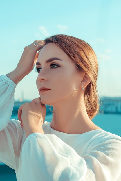 Portrait of beautiful young woman in long white dress standing on rooftop of building with cityscape