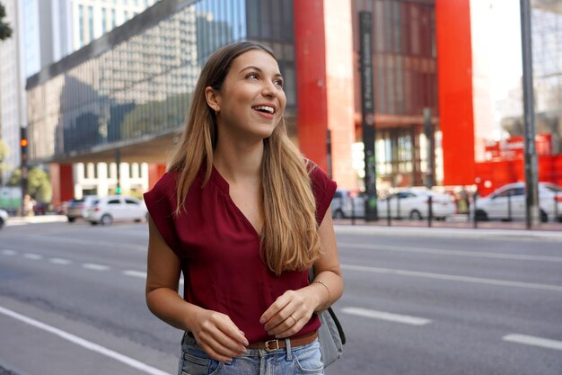 Photo portrait of beautiful young woman looking away on paulista avenue with masp museum on the background sao paulo brazil