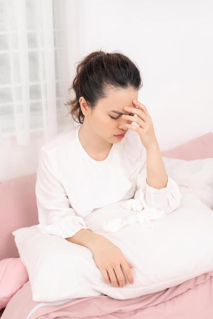 Portrait of a beautiful young woman lying in bed having a cold and sneezing in a tissue