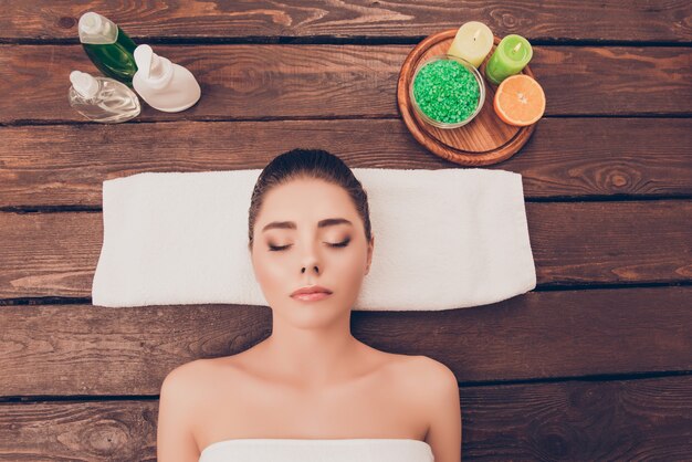 Portrait of beautiful young woman lying in sauna with lotions and candles