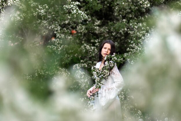 Photo portrait of a beautiful young woman in the park in the blooming branches at the summer or spring