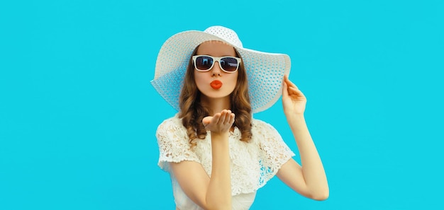 Portrait of beautiful young woman posing blowing lips sending sweet kiss in white summer straw hat