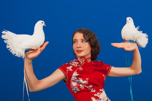 Portrait of a beautiful young woman in a red dress, in her hands two white pigeons