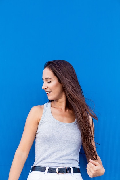 Portrait of a beautiful young woman smiling and playing with her hair with a blue background