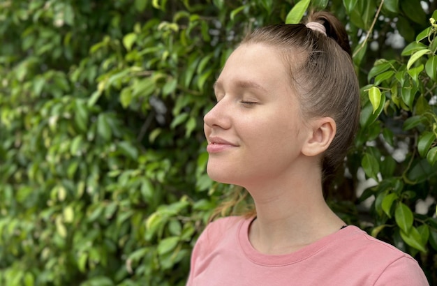 Portrait of a beautiful young woman standing on an Ivy wall or in greenery smiling and looking away against from plant girl relaxing outdoors during a sunny summer day Love for nature eco life