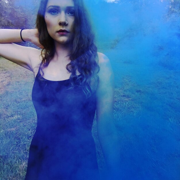 Portrait of beautiful young woman standing at park amidst smoke