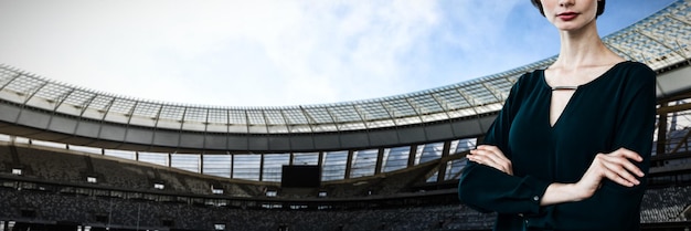 Portrait of beautiful young woman standing with arms crossed against rugby stadium on a sunny day