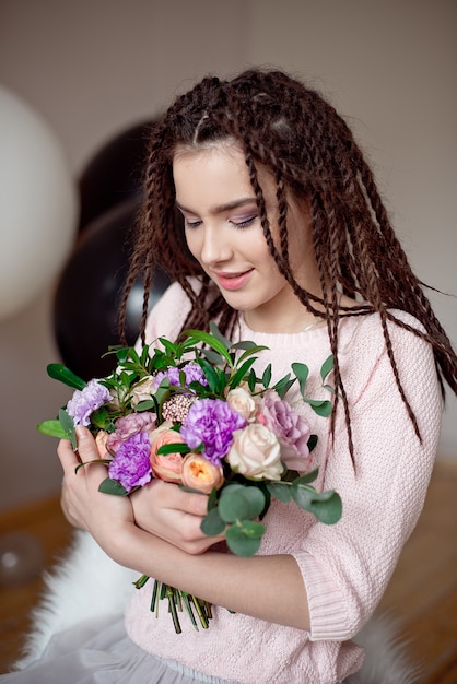 Foto ritratto di una bellissima giovane donna in un abito estivo e un cappello di paglia detiene un garofano, bouquet di rose e guardando oltre la sua spalla