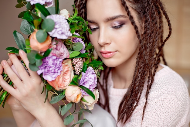 Foto ritratto di una bellissima giovane donna in un abito estivo e un cappello di paglia detiene un garofano, bouquet di rose e guardando oltre la sua spalla