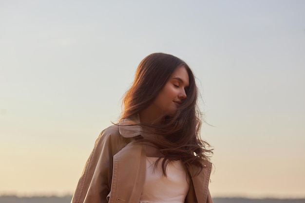 Portrait of a beautiful young woman at sunset Natural beauty long hair woman in a raincoat