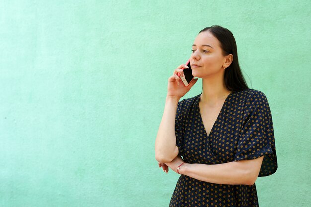 Портрет красивой молодой женщины разговаривает по телефону на зеленом фоне с копией пространства