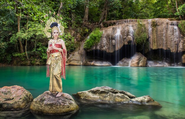 Foto ritratto di una bella giovane donna che indossa una corona e abiti tradizionali mentre è in piedi su una roccia contro il lago nella foresta