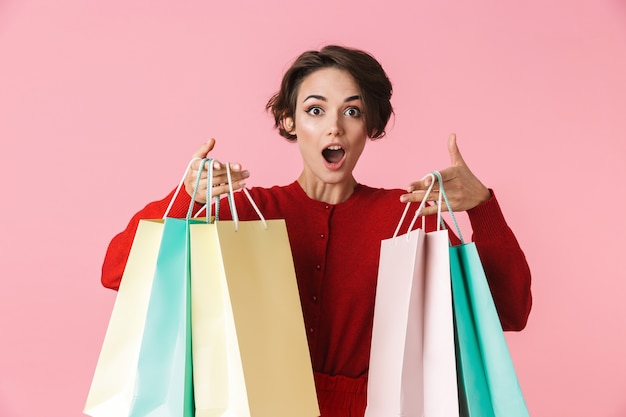 Portrait of a beautiful young woman wearing red clothes standing isolated, carrying shopping bags