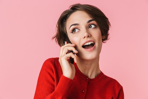 Портрет красивой молодой женщины в красной одежде, стоящей изолированно, разговаривает по мобильному телефону