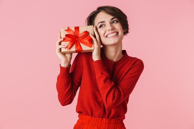 Portrait of a beautiful young woman wearing red dress standing isolated, holding gift box