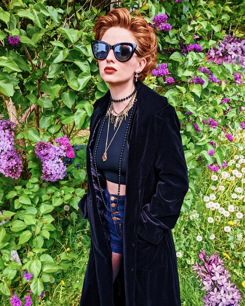 Portrait of beautiful young woman wearing sunglasses standing by flower plants