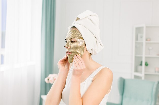 Photo portrait of beautiful young woman in white towel on the head with nude makeup and cosmetic paper gold mask on face.