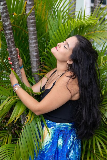 Photo portrait of beautiful young woman with black hair among leaves and branches of green plants posing for a photo