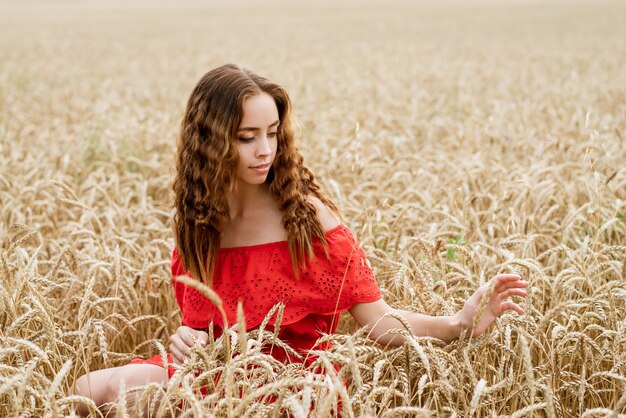 Ritratto di una bellissima giovane donna con i capelli ricci, seduto in un abito rosso in un campo di grano