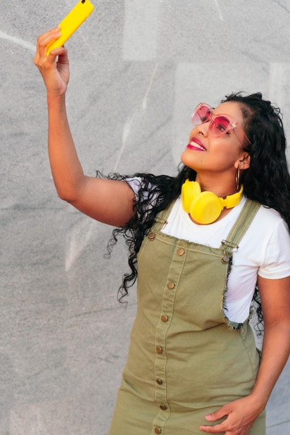 Portrait of a beautiful young woman with curly hair taking a selfie on the city street.