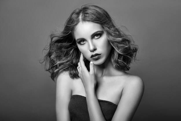 Portrait of a beautiful young woman with flying hair. Cute girl posing on a gray background. Big beautiful eyes and natural makeup. Long curly hair, perfect face.