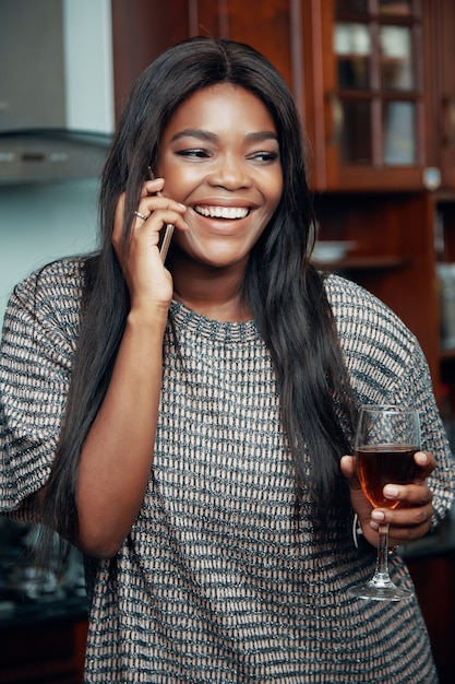 Portrait of beautiful young woman with glass of red wine laughing when taking on phone with best friend