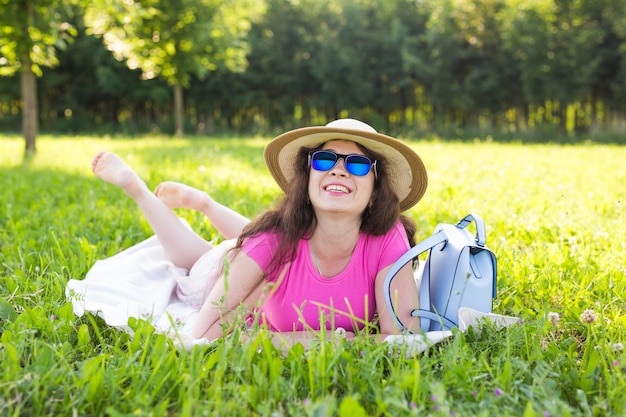 Портрет красивой молодой женщины в шляпе и солнцезащитных очках, лежа в парке на пикнике