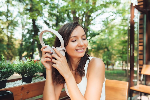 通りのカフェに座って音楽を聴くヘッドフォンを持つ美しい若い女性の肖像音楽ジェネレーション Z を楽しむ