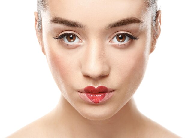 Portrait of beautiful young woman with heart painted on lips against white background