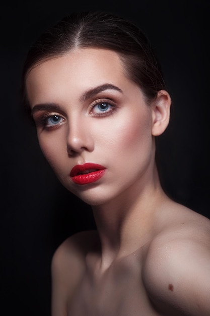 Portrait of beautiful young woman with perfect young skin and red lips on dark background