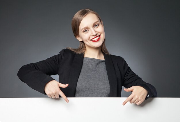 Portrait of beautiful young woman with red lips showing blank space with index finger