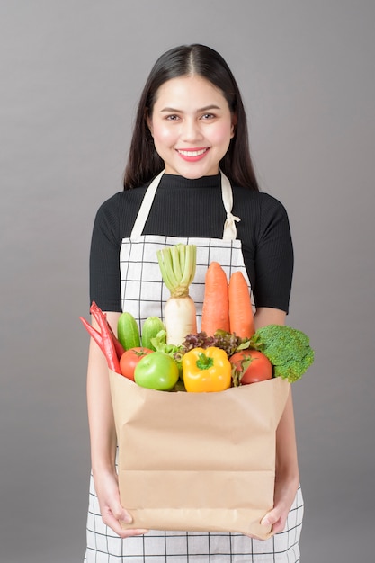 灰色のスタジオの背景に食料品の袋に野菜と美しい若い女性の肖像画