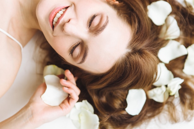 Portrait of beautiful young woman with white rose petal on white background. Relax and spa