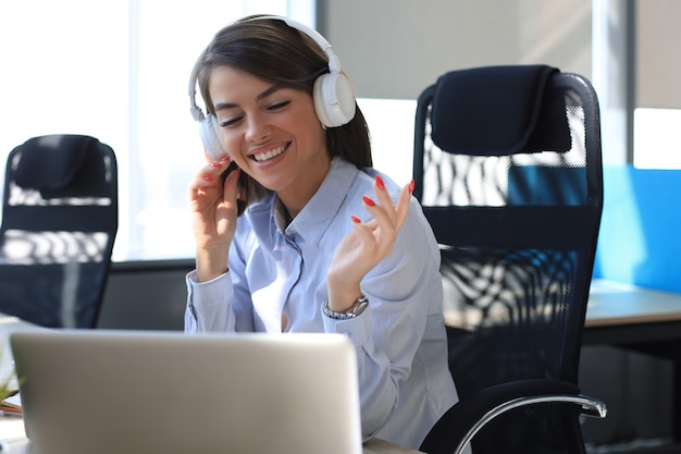 Portrait of beautiful young woman working on computer and chatting sitting in earphones.