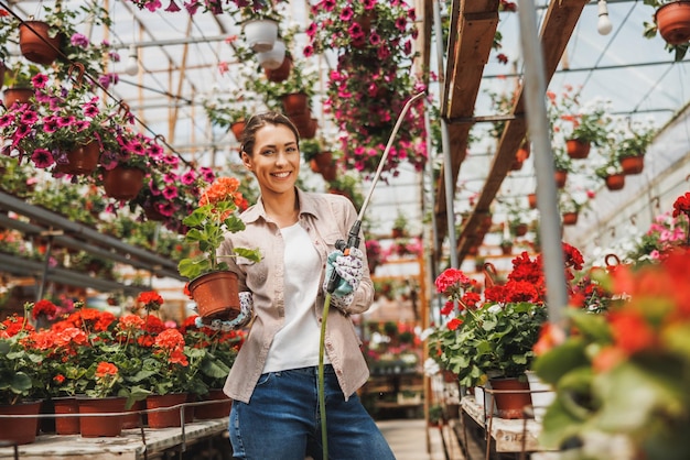 Portrait of a beautiful young woman working in flower greenhouse and looking at camera. Woman entrepreneur.