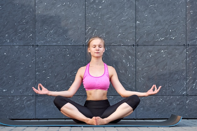 Portrait of beautiful young woman working out against grey wall, doing yoga or pilates exercise. Full length shot