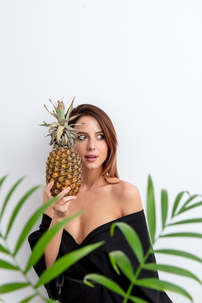 Портрет красивой женщины с ананасом и пальмовой ветвью на белом фоне