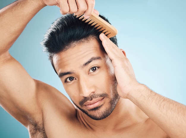 Photo portrait beauty and a man brushing his hair on a blue background in studio for self grooming face morning and routine with a young male model in the bathroom for style after shampoo treatment