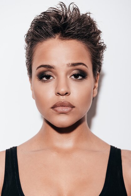 Portrait of beauty. Portrait of beautiful young short hair woman in black tank top looking at camera while standing against white background