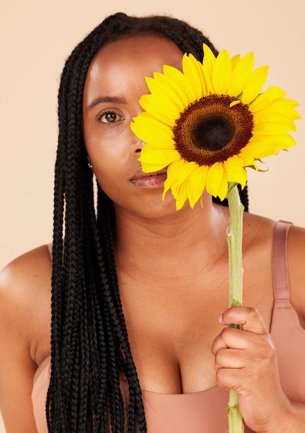 Portrait beauty and sunflower with a black woman in studio on a beige background for natural treatment or body positivity Spring flower and skincare with a young female posing for wellness