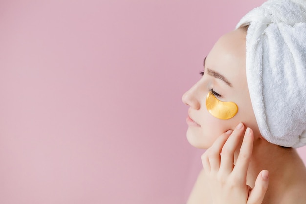 Ritratto di donna di bellezza con bende per gli occhi su sfondo rosa donna di bellezza viso con maschera sotto gli occhi bella donna con trucco naturale e cosmetici dorati patch di collagene sulla pelle del viso fresca