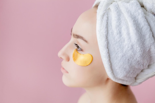 Portrait of Beauty Woman with Eye Patches on pink background Woman Beauty Face with Mask under Eyes Beautiful Female with natural Makeup and Gold Cosmetics Collagen Patches on Fresh Facial Skin